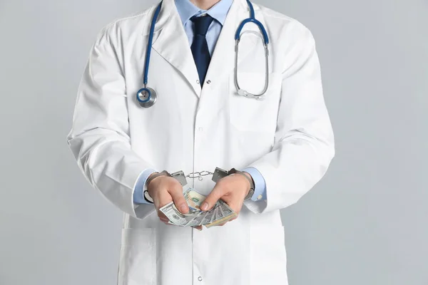 Lekarz w kajdankach z łapówką na szarym tle, zbliżenie. Korona — Zdjęcie stockowe
