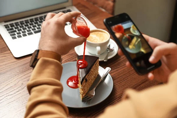 Чоловічий блогер фотографує десерт і каву за столом у кафе — стокове фото