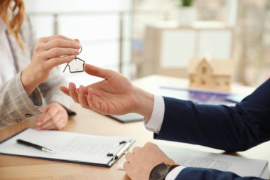 Real estate agent giving key with trinket to client in office, c