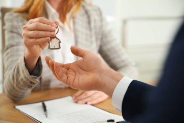 Real estate agent giving key with trinket to client in office, c