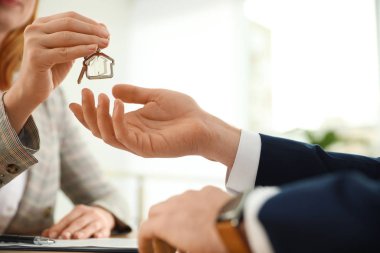 Real estate agent giving key with trinket to client in office, c