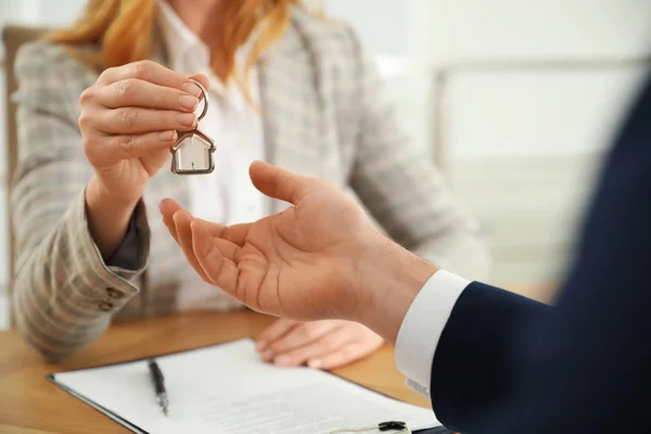 Real estate agent giving key with trinket to client in office, c — 스톡 사진