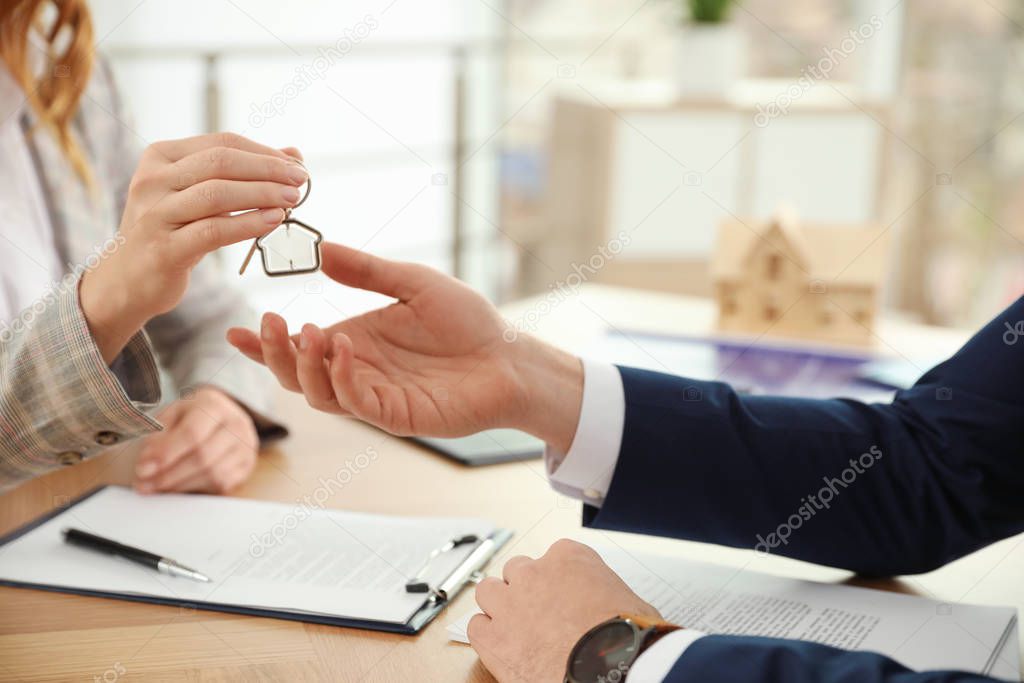 Real estate agent giving key with trinket to client in office, c