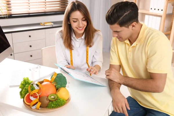 Young nutritionist consulting patient at table in clinic — Stock Photo, Image