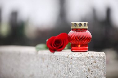 Red rose and candle on light grey granite tombstone outdoors. Fu