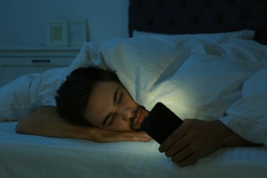Genç adam gece yatakta akıllı telefona bağımlı.