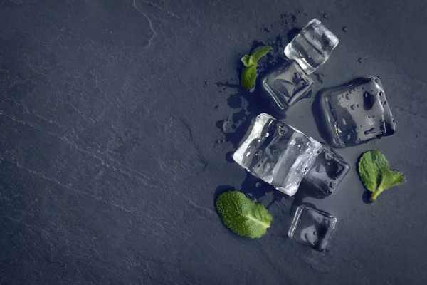 Crystal clear ice cubes with water drops and mint on black table, flat lay. Space for text