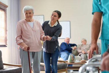 Care worker helping to elderly woman with stick in geriatric hos