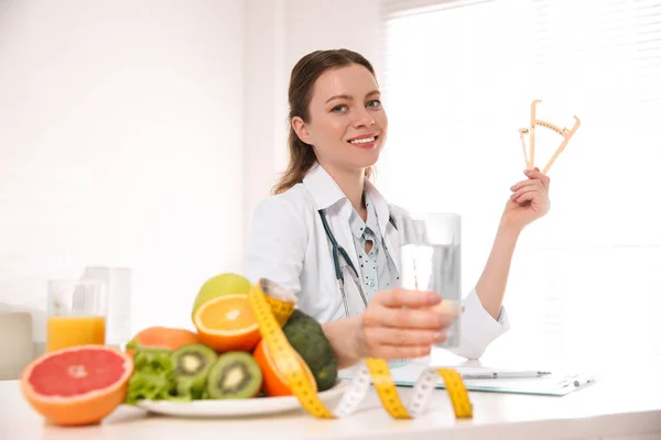 Nutricionista con pinza y vaso de agua en escritorio en oficina — Foto de Stock