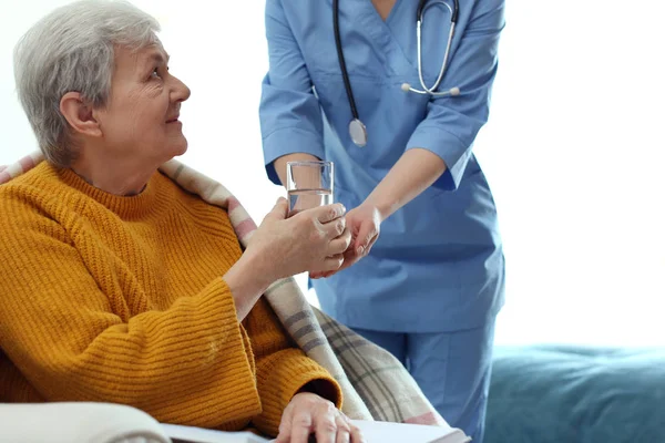 Cuidador que dá água à mulher idosa em hospício geriátrico — Fotografia de Stock