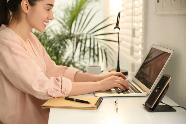 Femme travaillant à table tandis que son téléphone portable charge avec du fil — Photo