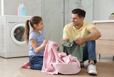 Banyoda temiz çamaşırları olan baba ve küçük kızı.