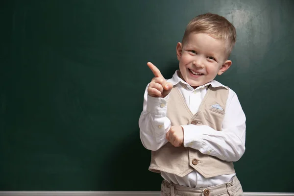 Pequeño niño divertido cerca de pizarra, espacio para el texto. Primera vez a —  Fotos de Stock