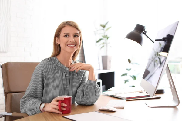 Mujer joven con taza de bebida relajarse en la mesa en la oficina durante — Foto de Stock