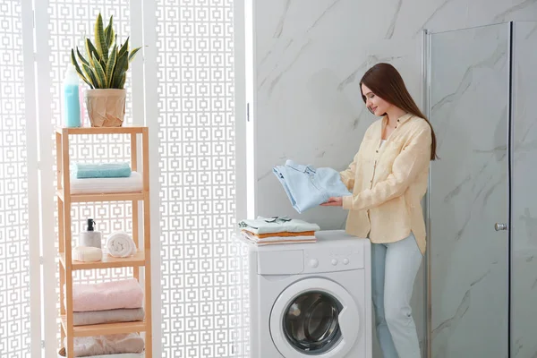 Mulher feliz com roupas limpas perto da máquina de lavar roupa no banheiro . — Fotografia de Stock