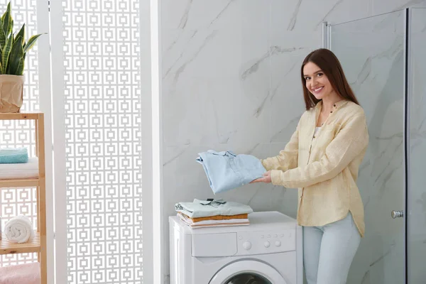 Щаслива жінка з чистим одягом біля пральної машини у ванній . — стокове фото
