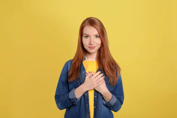 Beautiful grateful woman with hands on chest against yellow back — 图库照片