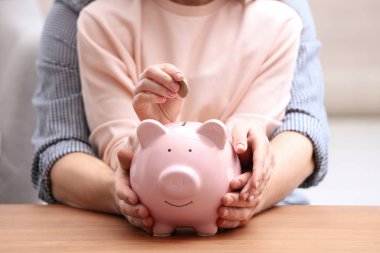 Couple with piggy bank and coin at wooden table, closeup
