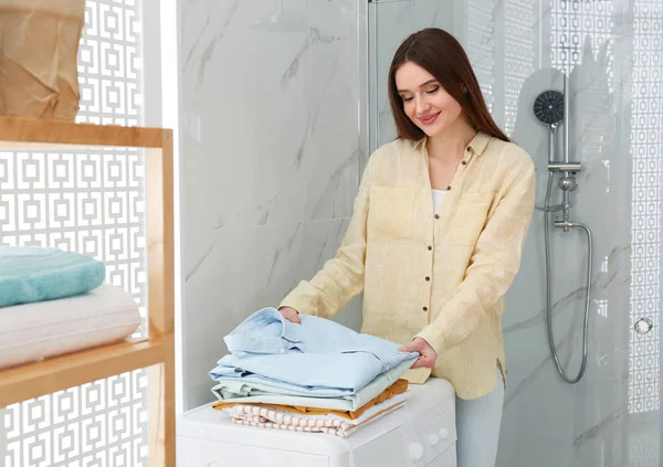 Mulher feliz com roupas limpas perto da máquina de lavar roupa no banheiro . — Fotografia de Stock