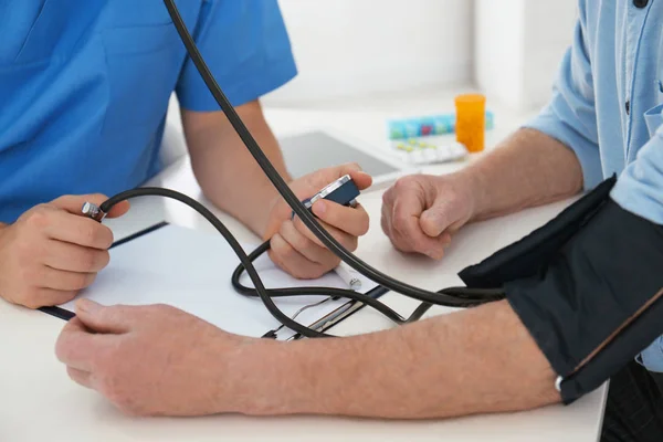Médico midiendo la presión arterial del paciente mayor en el consultorio, clo — Foto de Stock
