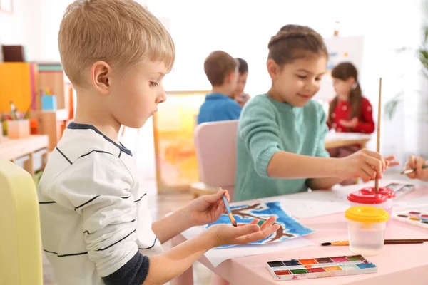 Bonito crianças pintando as palmas das mãos à mesa no quarto — Fotografia de Stock