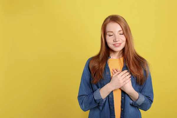 Beautiful grateful woman with hands on chest against yellow back — 图库照片