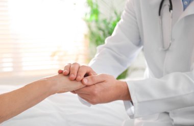 Doktor ve kıdemli hasta hastanede el ele tutuşuyor.
