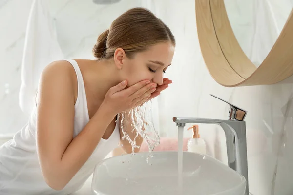 Jonge vrouw wassen gezicht met kraanwater in de badkamer — Stockfoto