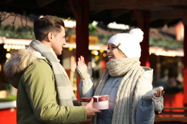 Man presenting Christmas gift to his girlfriend at winter fair