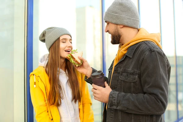Милая молодая пара с бутербродом и кофе на городской улице — стоковое фото