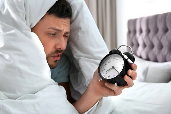 Slaperige man met wekker thuis in de ochtend — Stockfoto