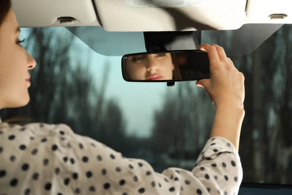 Młoda kobieta dostosowująca lusterko wsteczne w samochodzie, zbliżenie — Zdjęcie stockowe