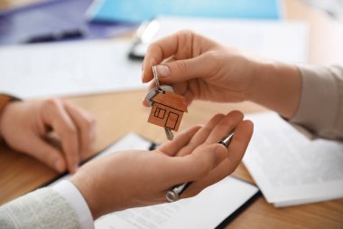Real estate agent giving key with trinket to client in office, c