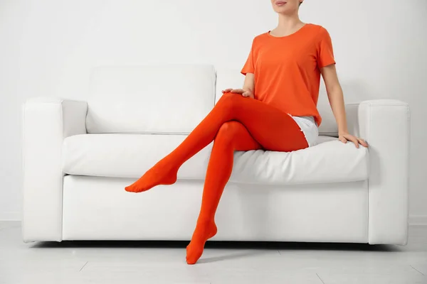 身穿橙色紧身衣的妇女坐在室内沙发上 — 图库照片