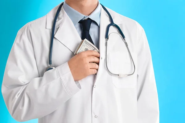 Doctor putting bribe into pocket on light blue background, close — Stock Photo, Image