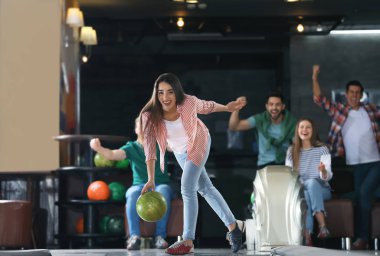 Genç bir kadın top oynuyor ve arkadaşlarıyla bowling kulübünde vakit geçiriyor.