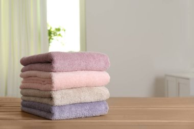 Stack of fresh towels on wooden table in bathroom. Space for text