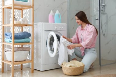 Banyoda çamaşır makinesinin yanında elbiseleri olan genç bir kadın. Laund