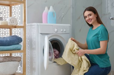 Banyoda çamaşır makinesinin yanında elbiseleri olan genç bir kadın. Laund