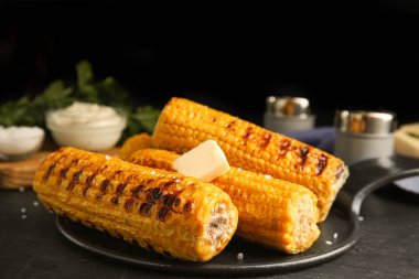 Lezzetli ızgara mısır koçanları siyah masada.