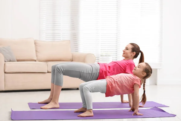 Madre joven con hija pequeña practicando yoga en casa —  Fotos de Stock