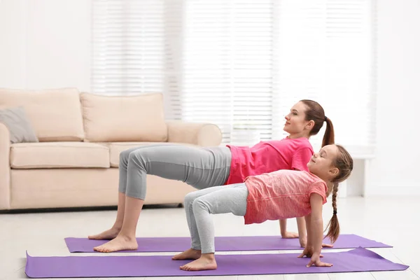 Madre joven con hija pequeña practicando yoga en casa — Foto de Stock