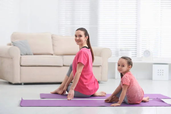 Madre joven con hija pequeña practicando yoga en casa — Foto de Stock