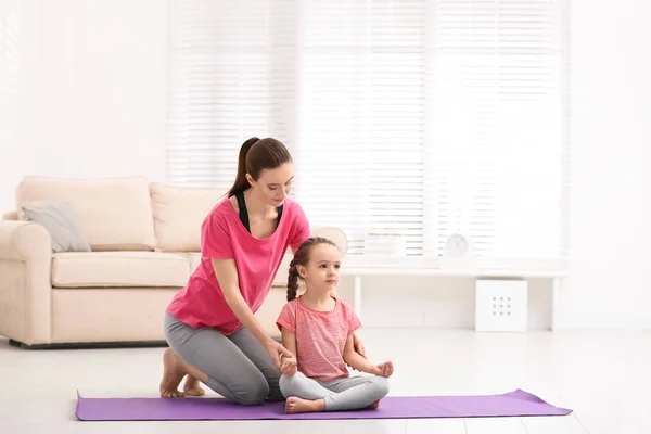 Madre joven con hija pequeña practicando yoga en casa — Foto de Stock