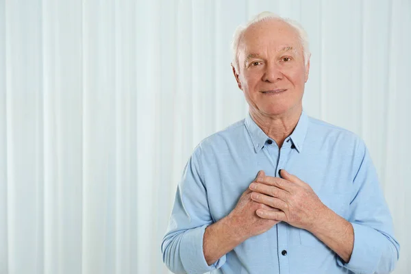 Vděčný starší muž s rukama na hrudi na světlém pozadí — Stock fotografie