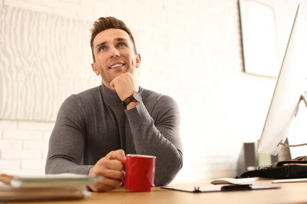 Молодий чоловік з чашкою напою розслабляється за столом в офісі під час б — стокове фото