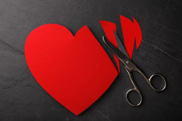 Cut paper heart and scissors on black stone background, flat lay