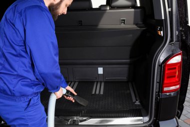 Otomobil bagajında elektrikli süpürge kullanan bir işçi.