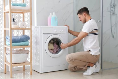 Banyoda çamaşır makinesinin yanında bir adam var. Çamaşır günü