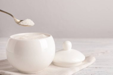 Tahta masadaki seramik kaseden bir kaşık beyaz şeker alıyorum. Evet.